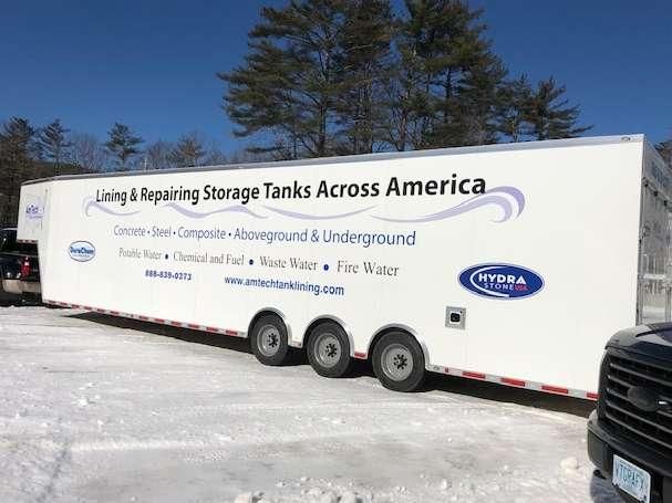 A white trailer is parked in the snow next to a truck.