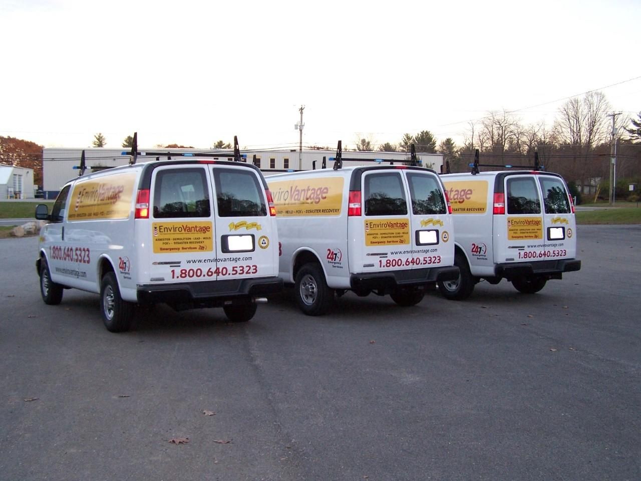 Three white vans are parked next to each other with a phone number on the back