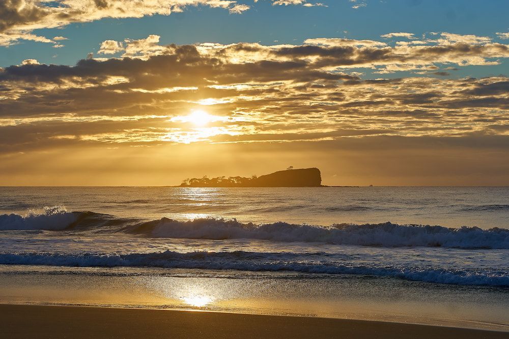 The Sun is Setting Over the Ocean With a Small Island in the Distance — Coolum Cutting Edge in Mudjimba, QLD