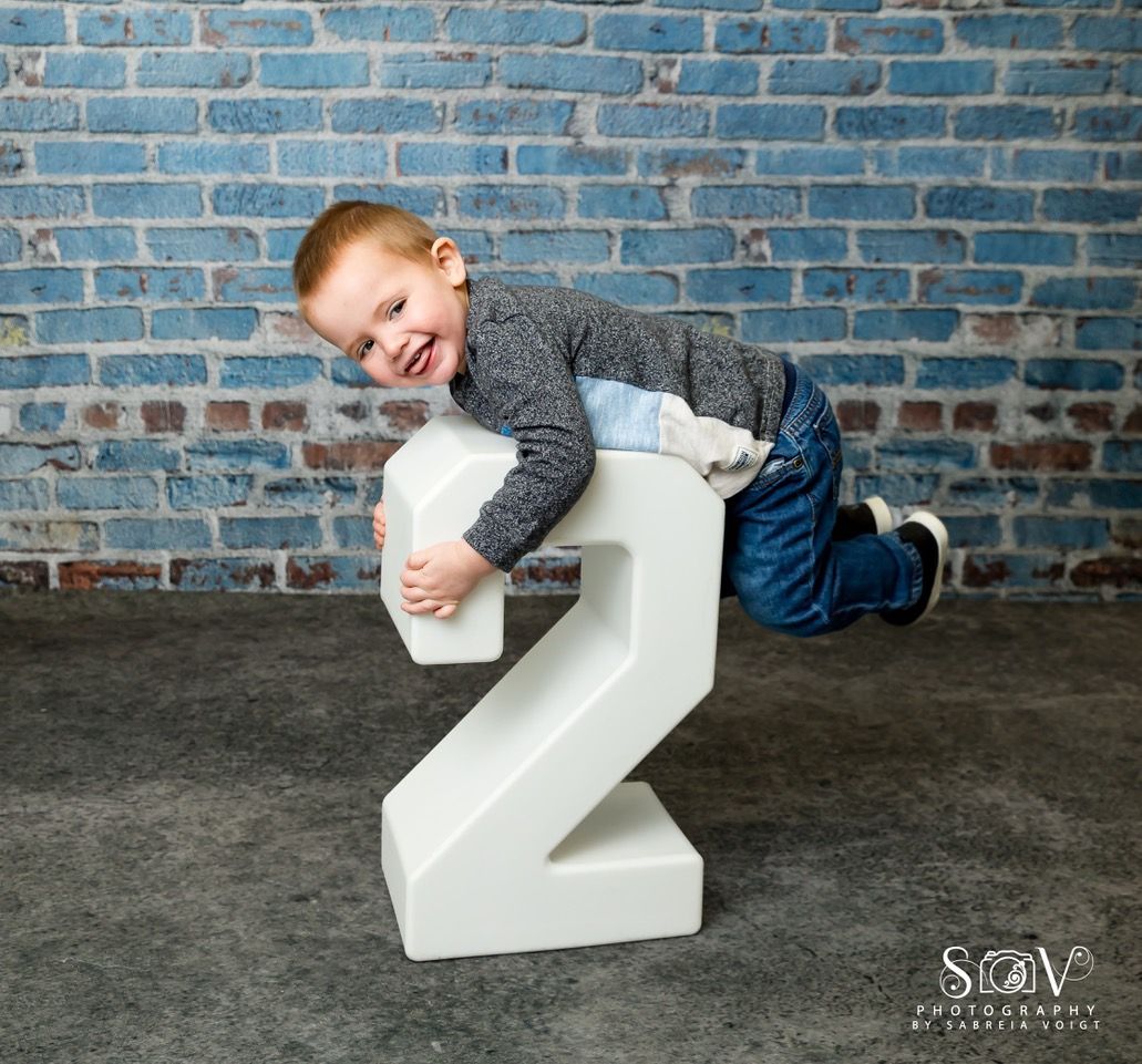 Boy smiles, leaning on a large white number 