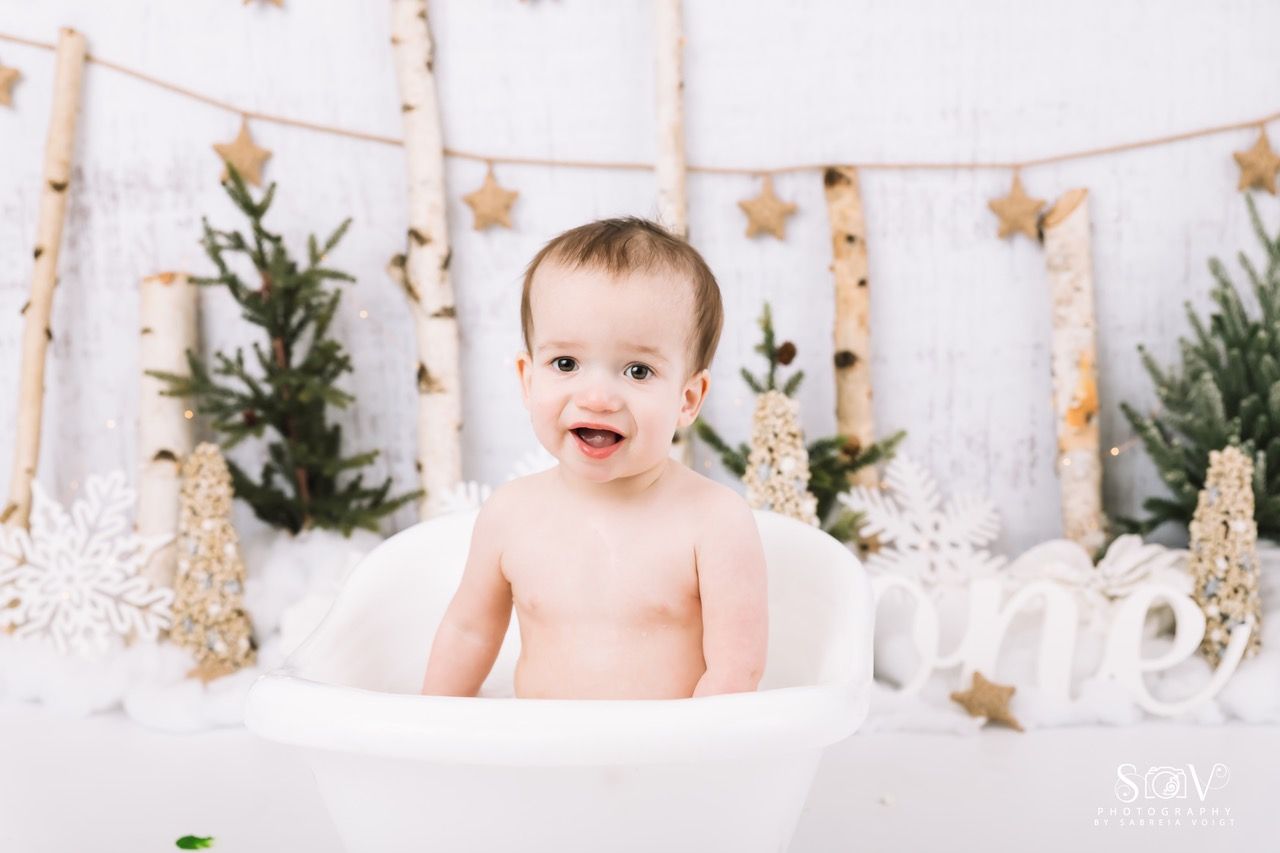 Baby in a white tub, smiling, in a winter-themed birthday setting.