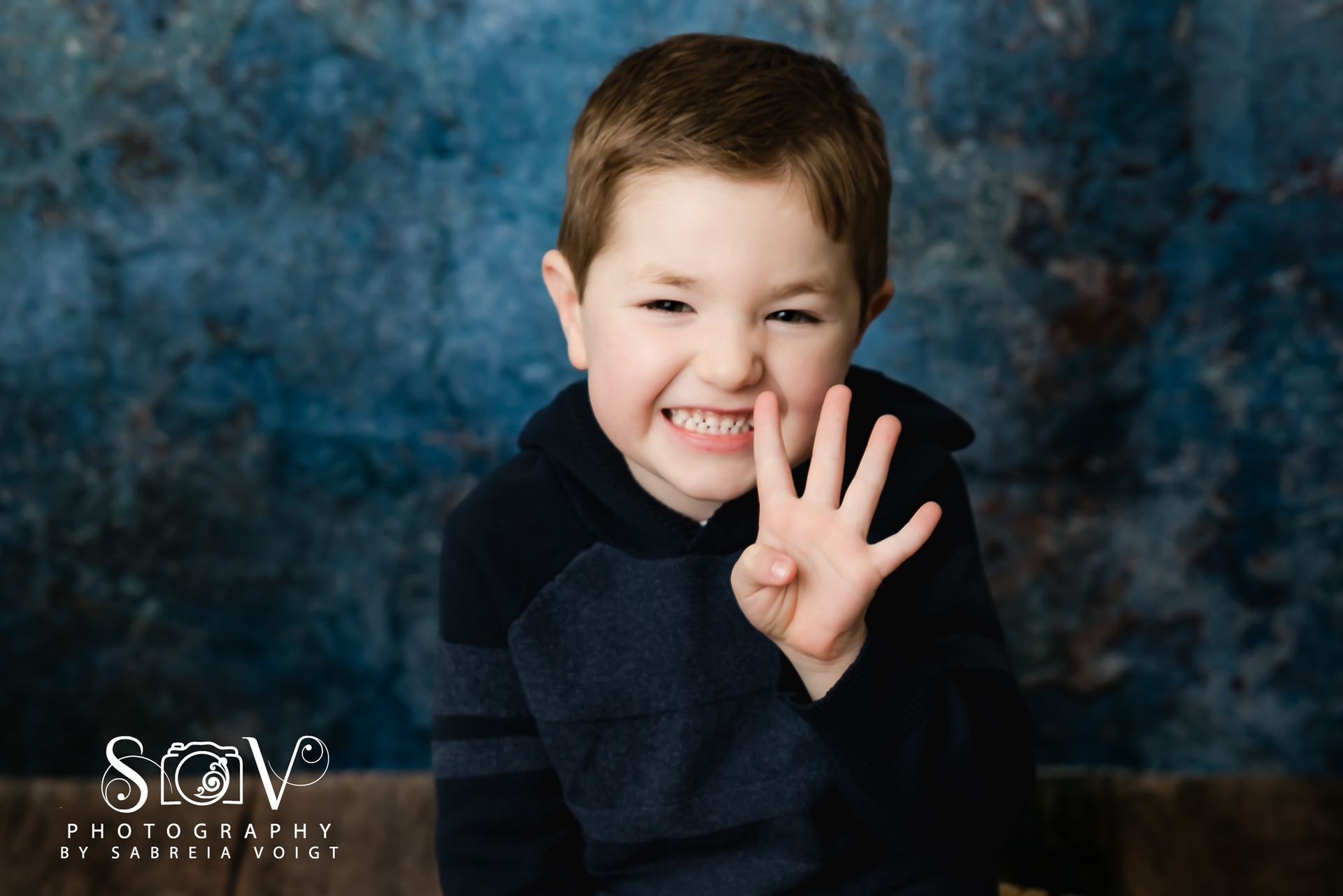 Young child with a happy expression holding up four fingers against a blue backdrop.