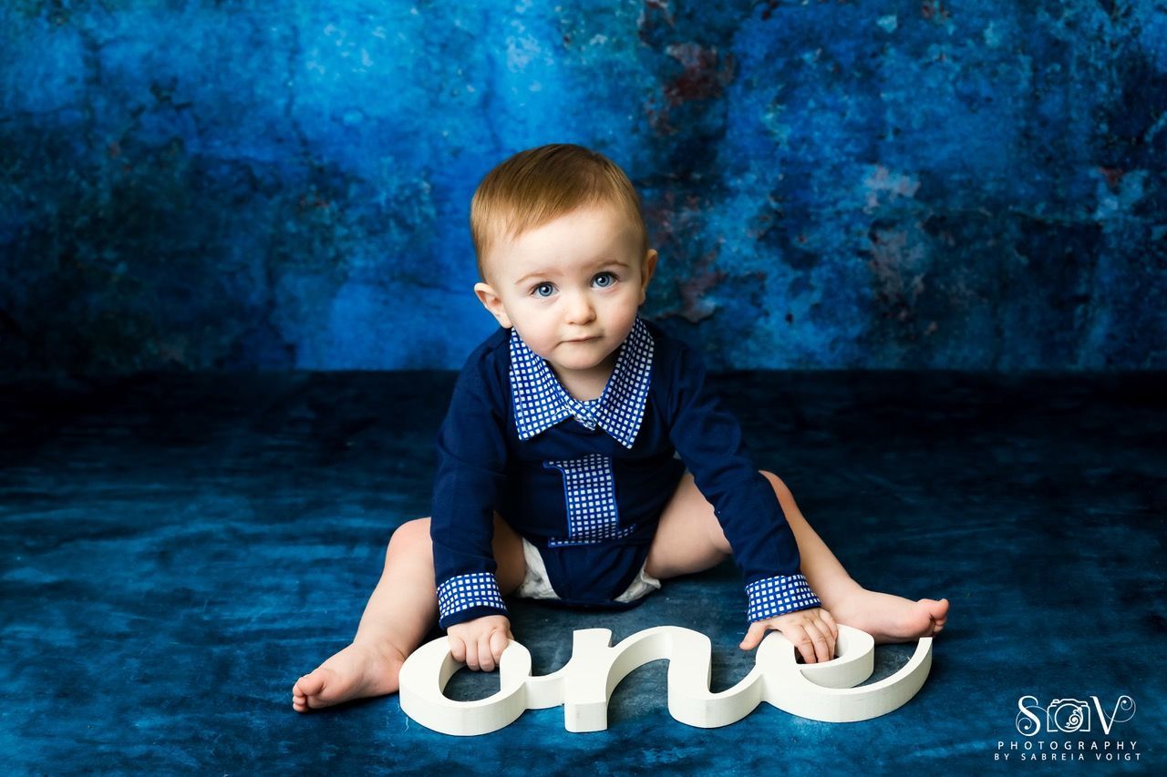 A baby in a blue outfit sits with the word 