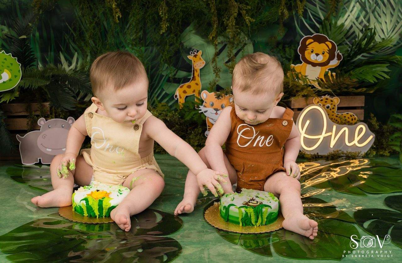 Two babies with green frosting on their hands, at a jungle-themed birthday celebration with small cakes.