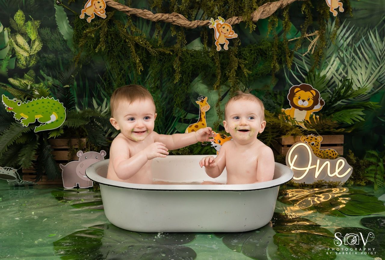 Two babies in a tub smile in a jungle-themed set. A 