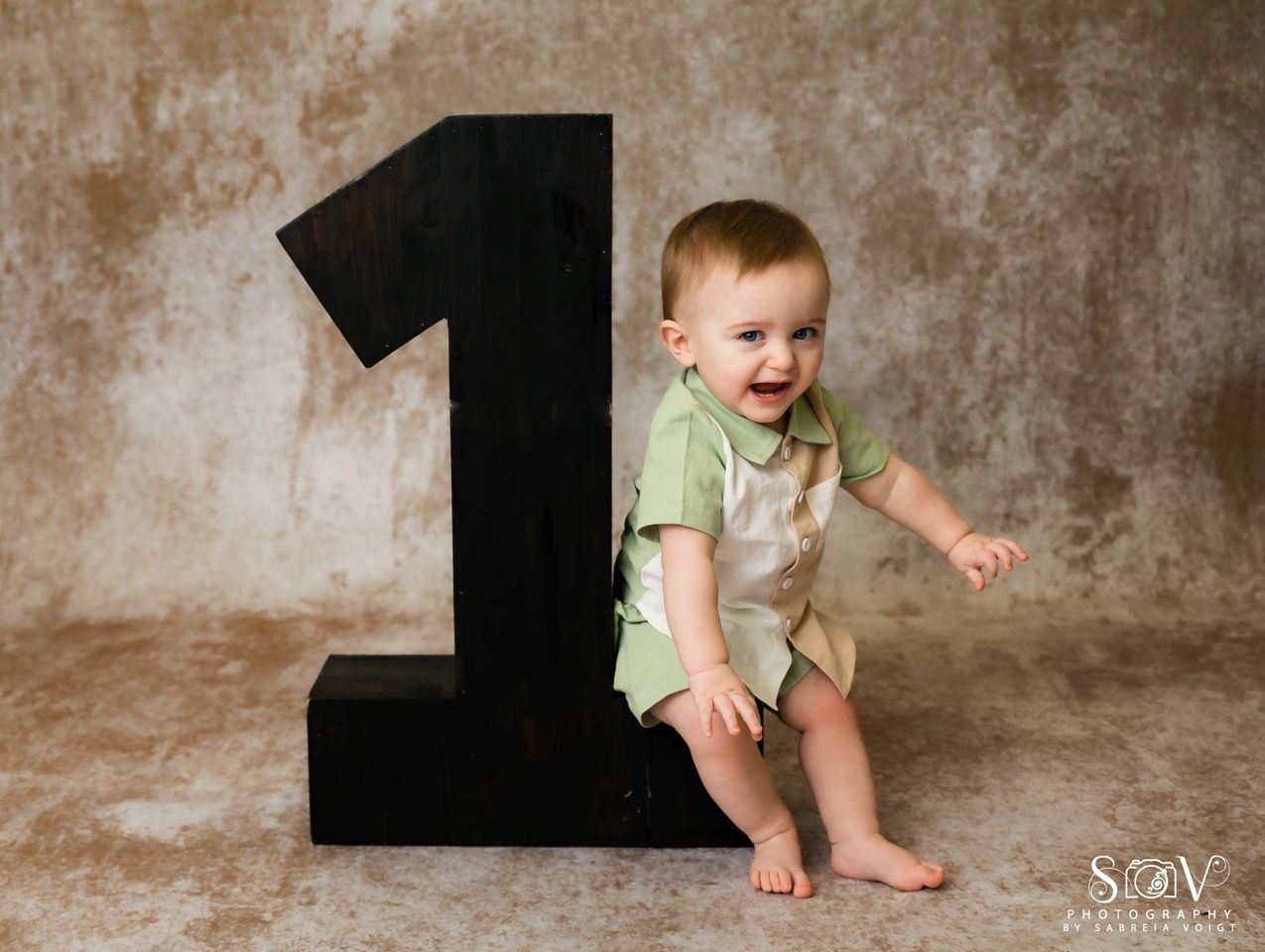 Smiling baby sits next to a large black number 