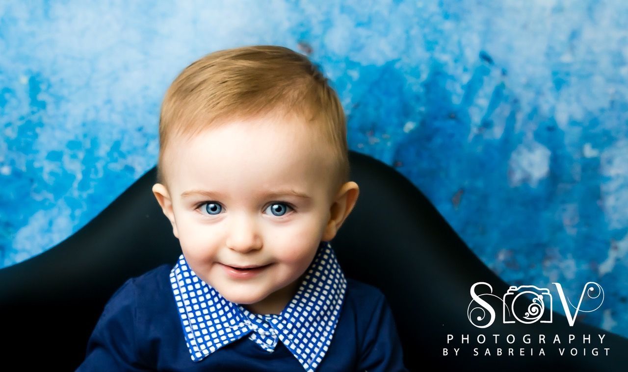 Smiling baby with blue eyes and a blue patterned collar against a blue background.