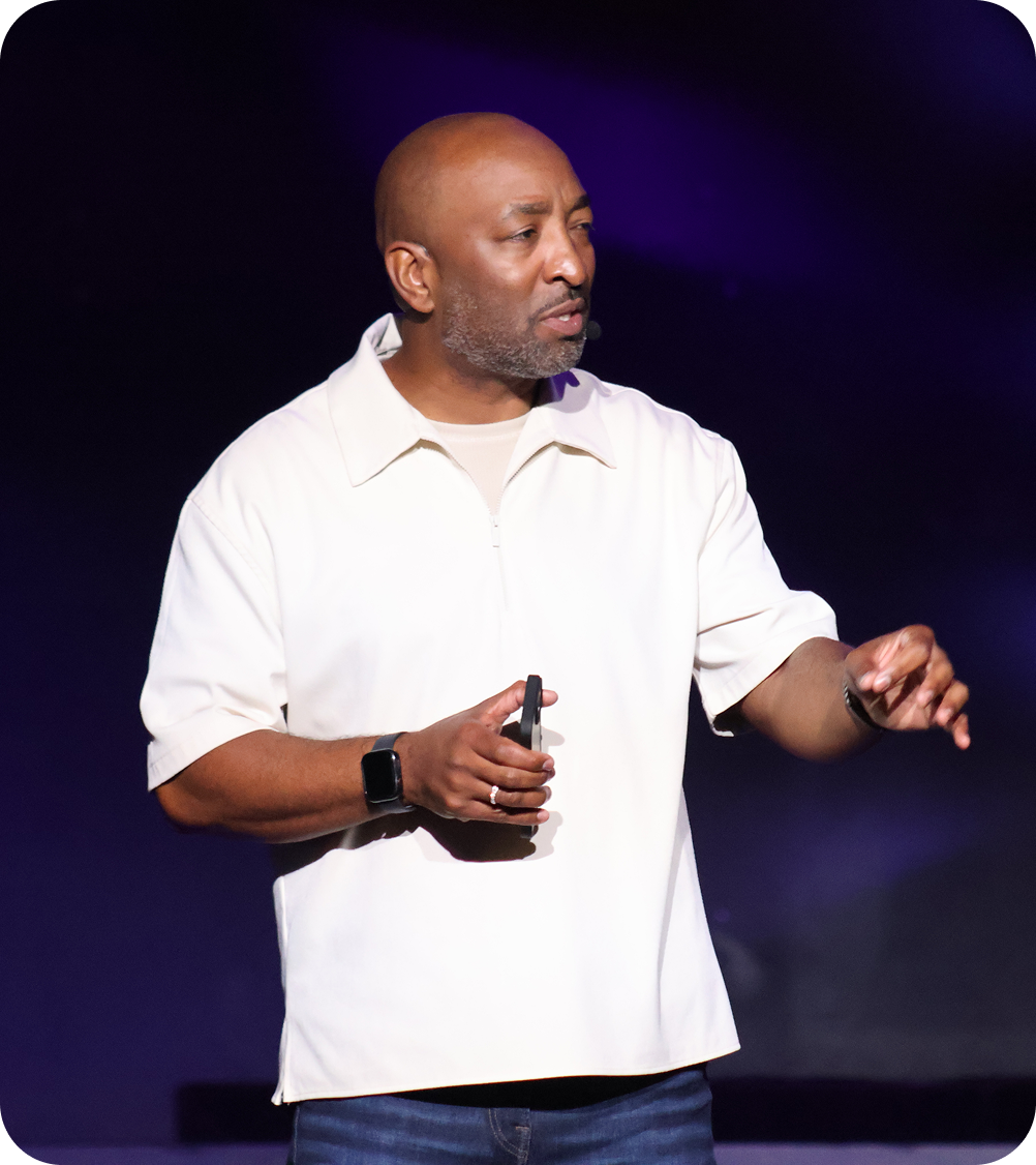 Man in a white shirt gesturing on a dark stage under purple lighting