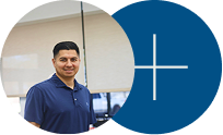 Man in a navy shirt standing beside a blue circle with a white plus sign in an office setting