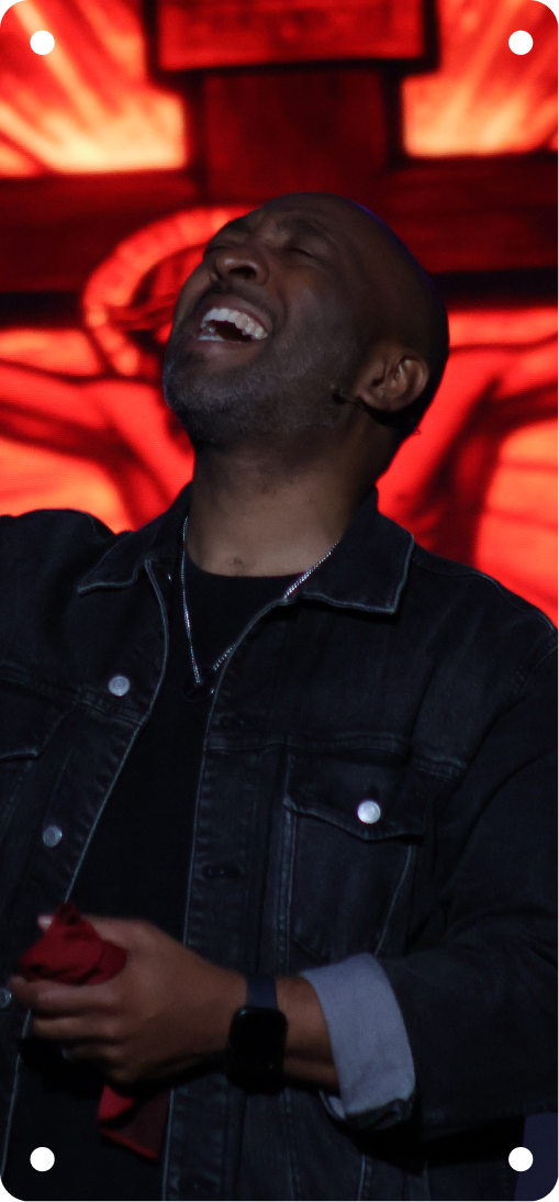 Smiling man in a dark jacket holding a red cup under red stage lights