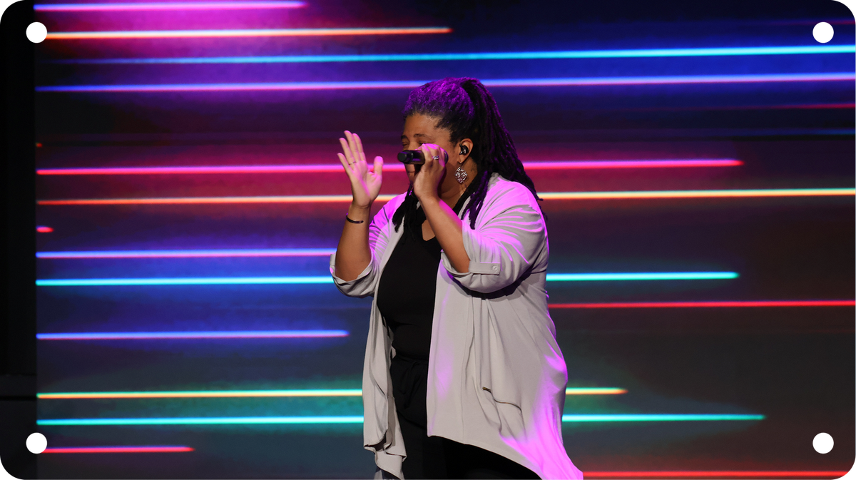 Singer performing on stage with neon horizontal lights, clapping and singing into a microphone