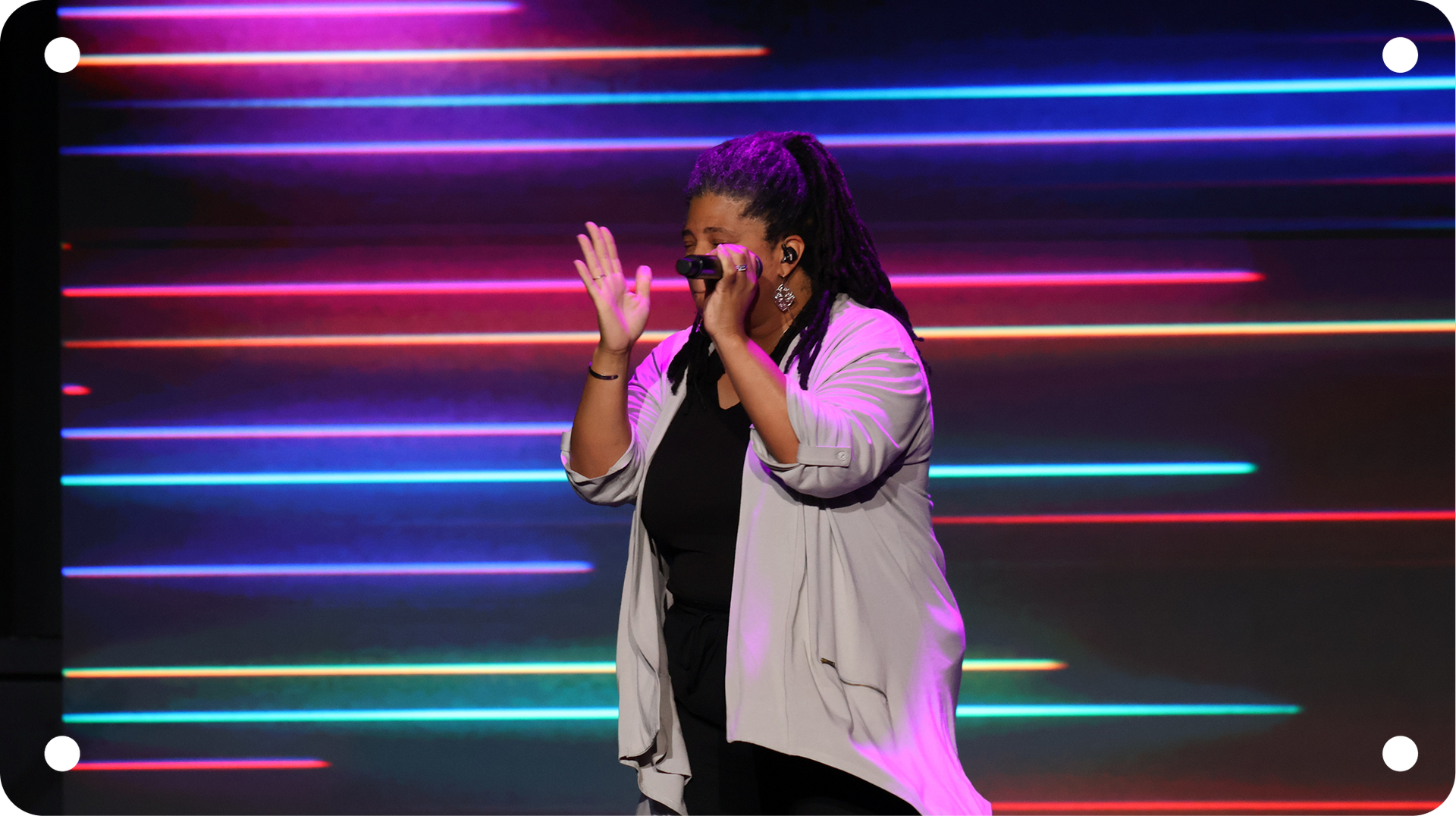 Singer performing on stage with neon horizontal lights, clapping and singing into a microphone