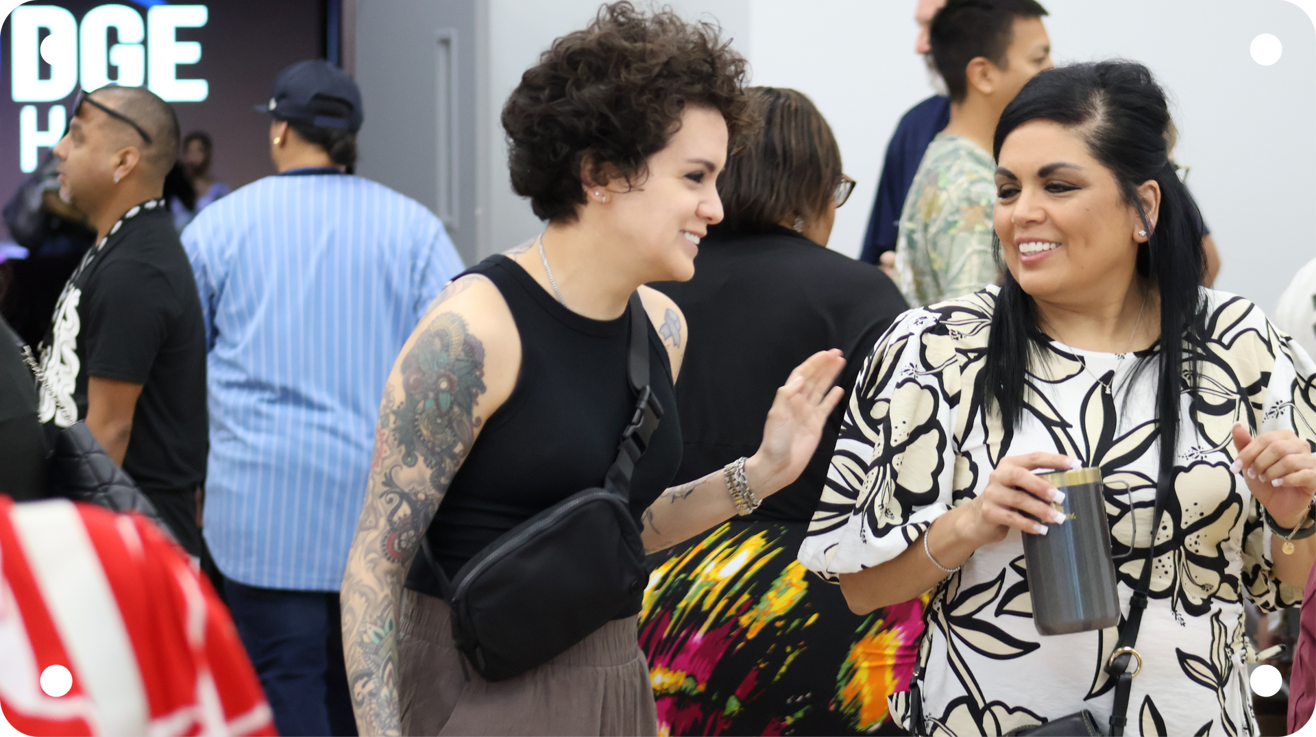Two women chatting and smiling at an outdoor event, one in a black top and the other holding a cup.