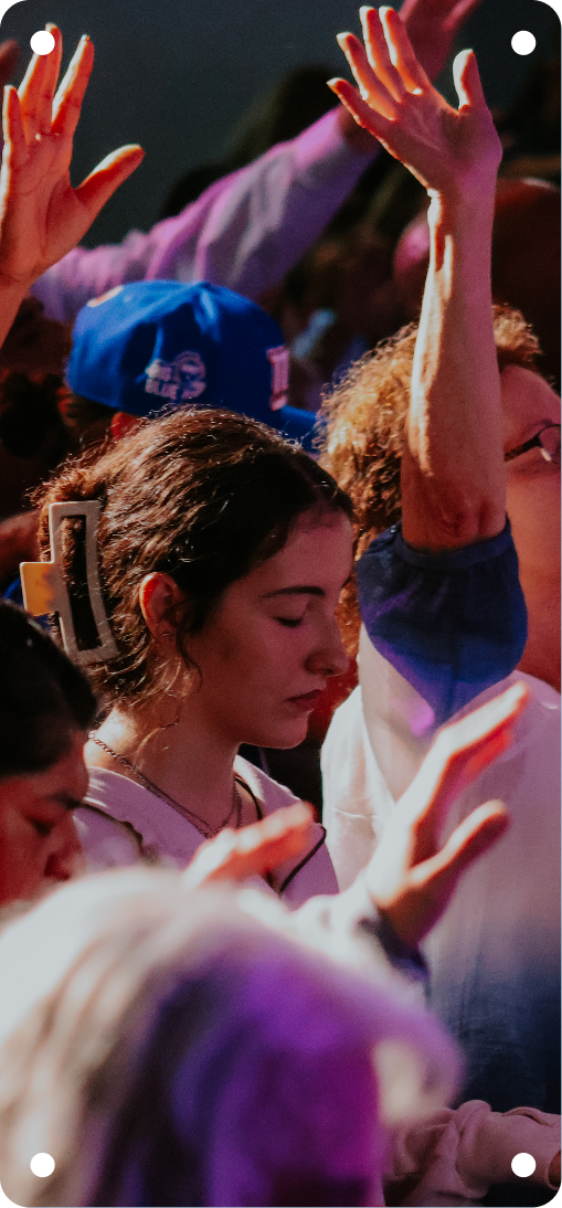 Crowd with raised hands under colorful stage lighting, one person in profile in the foreground