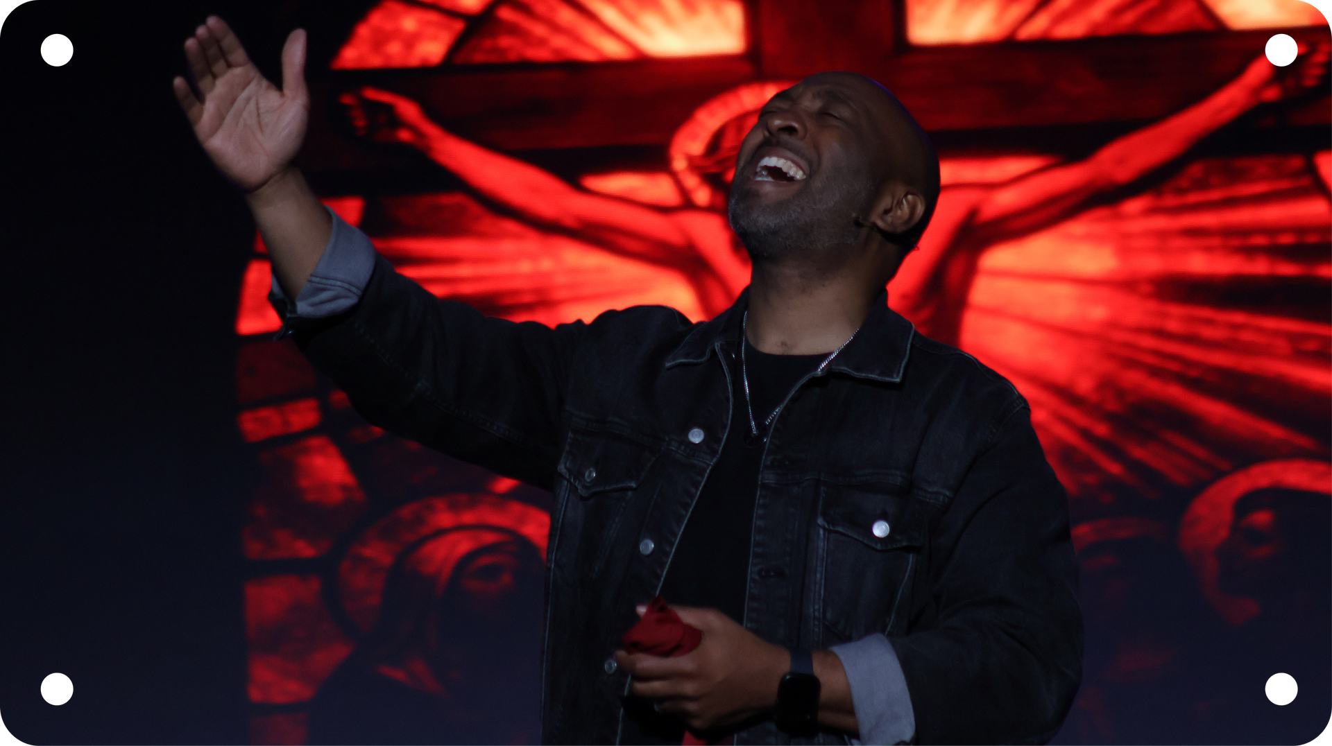 Man singing on stage with raised hand, lit by red abstract background lights