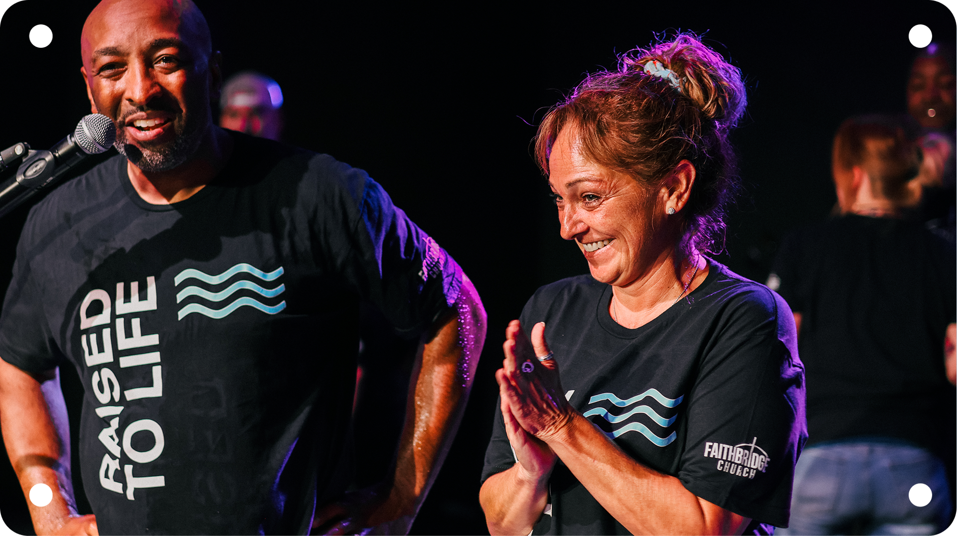 Two runners in black T-shirts with “Race for Life” logos smiling on a dark stage