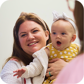 Smiling adult holding a baby in a yellow polka-dot outfit and white headband