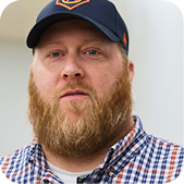 Man in a navy cap and plaid shirt with a beard, facing forward against a plain white background
