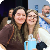 Two smiling people posing indoors, one holding a light blue tumbler mug