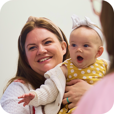 Woman holding a baby in a yellow polka-dot outfit with a surprised expression