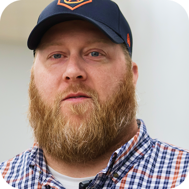 Bearded man in a navy cap and plaid shirt, looking at the camera.