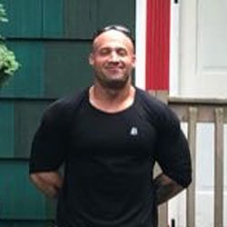 A man in a black shirt and sunglasses is standing in front of a house.
