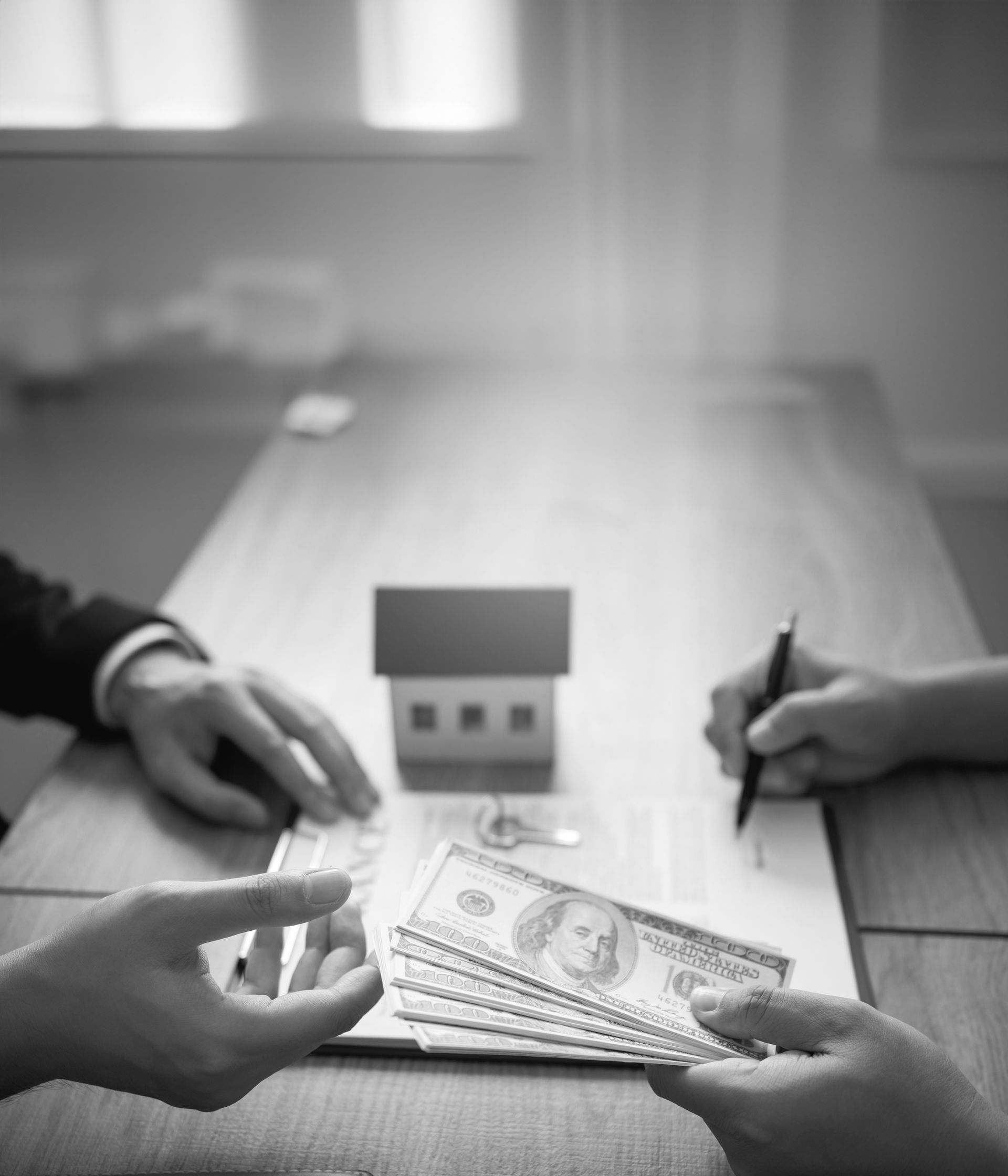 A black and white photo of two people sitting at a table with money and a model house.