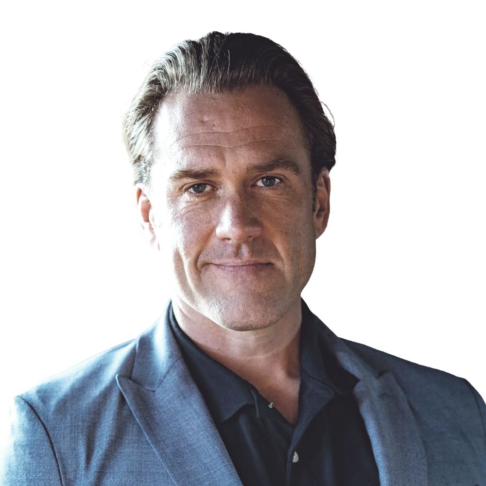 A man in a suit and black shirt is smiling for the camera