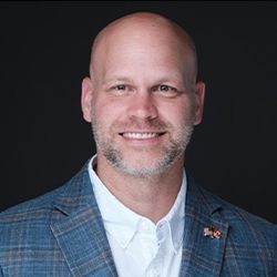 A bald man with a beard is wearing a suit and smiling.