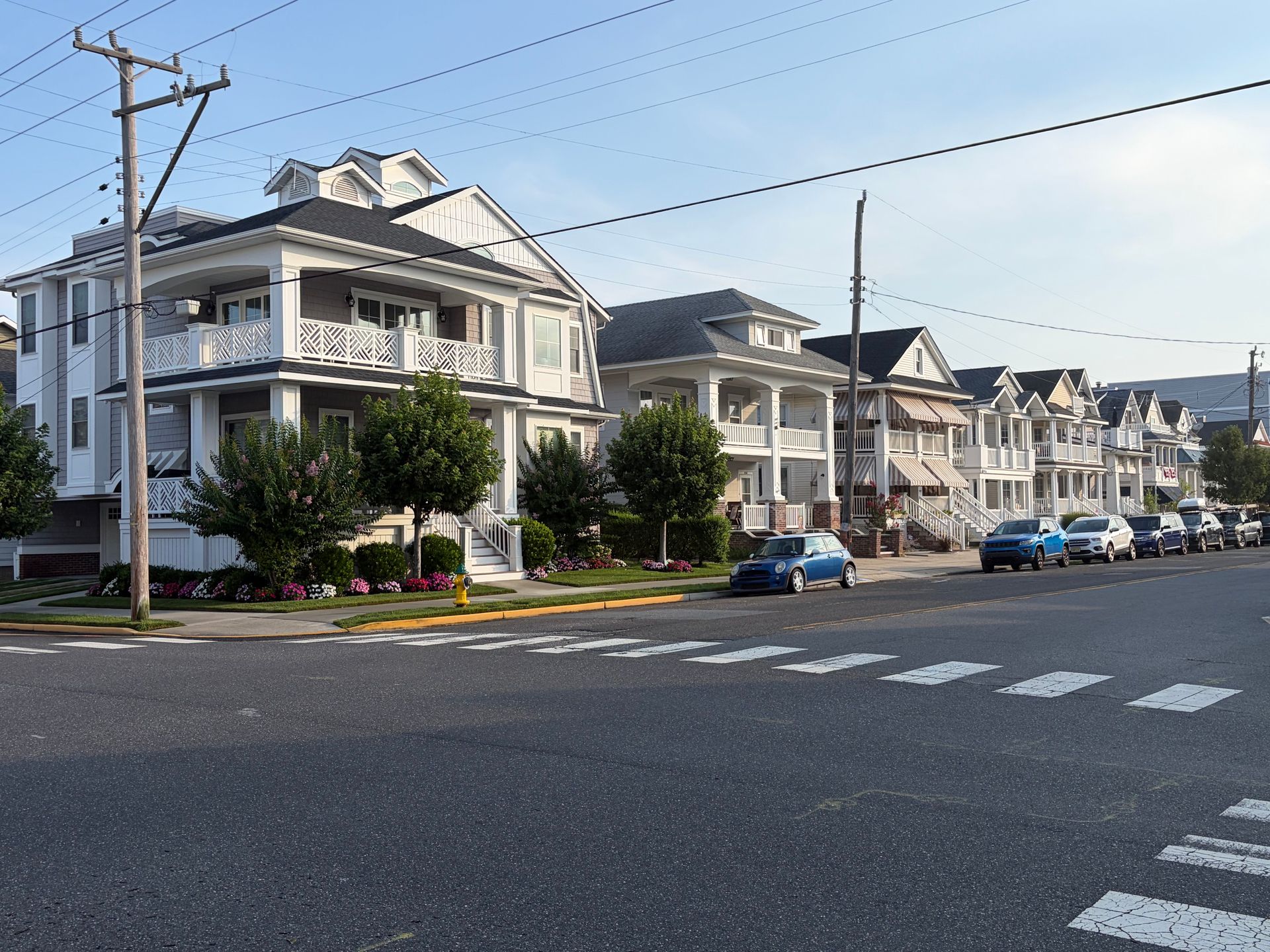 Suburban street with gray houses, parked cars, and a crosswalk under a clear sky