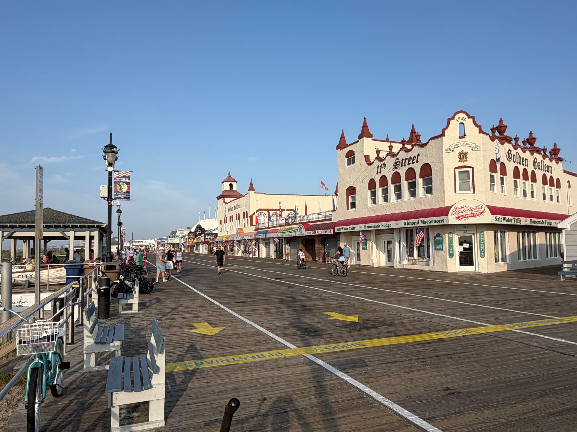 Boardwalk street scene with ornate white buildings, bicycles, and a cloudy sky by the waterfront.