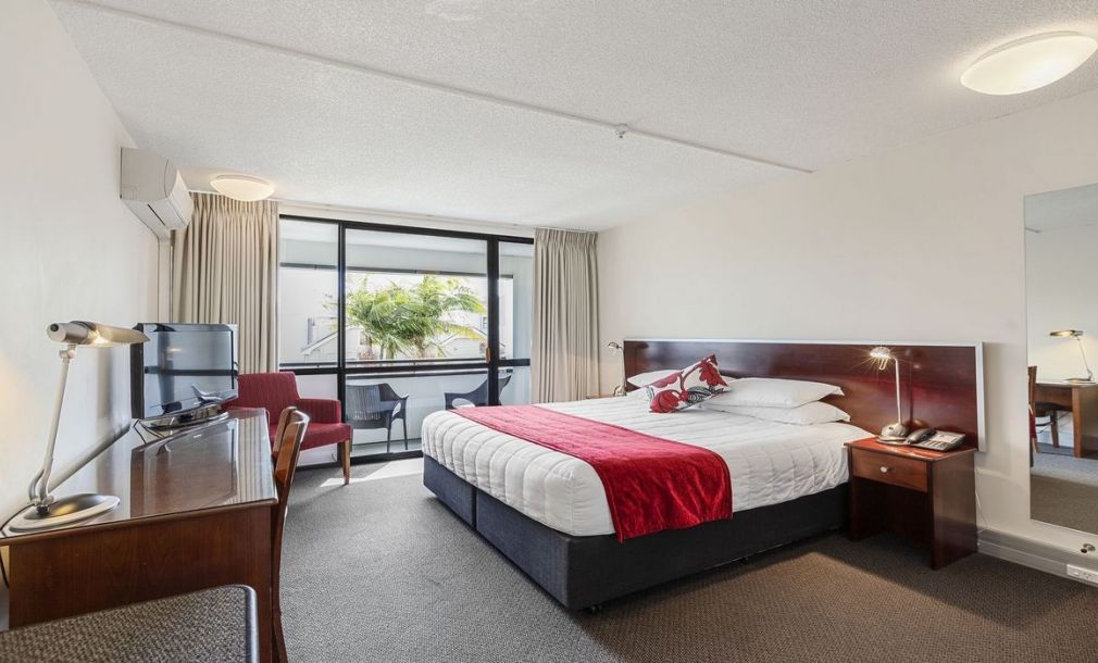 Modern hotel room with a large bed, red accent blanket, and balcony view through wide windows