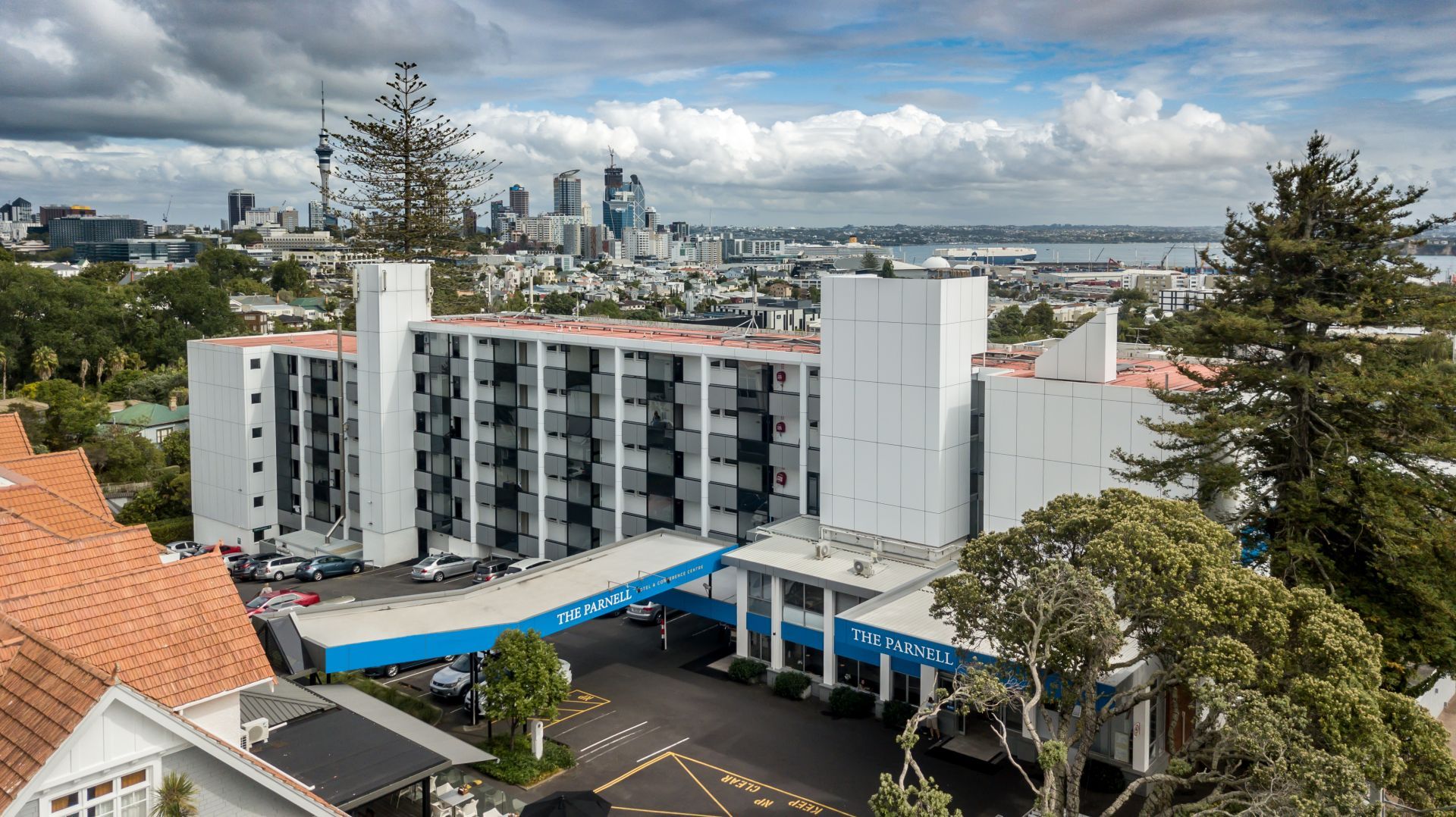 City skyline view over a white apartment building with blue awnings and trees in the foreground