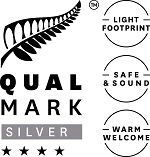 QUALMARK Silver logo with fern leaf, stars, and badges reading light footprint, safe & sound, warm welcome
