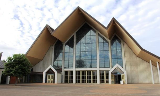 Modern church with tall glass facade and steep wooden roof under a cloudy sky