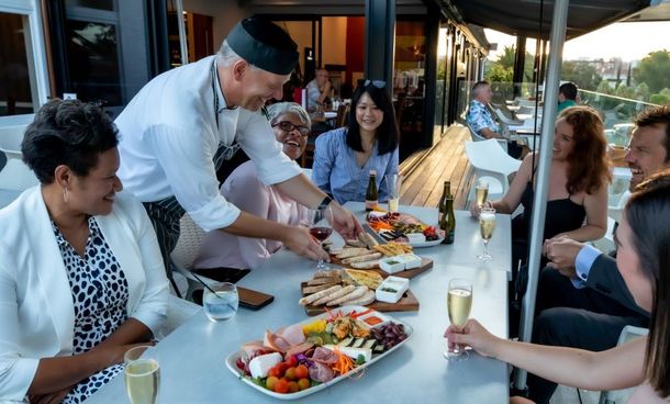 Outdoor dinner gathering with a chef serving food at a long table of smiling guests