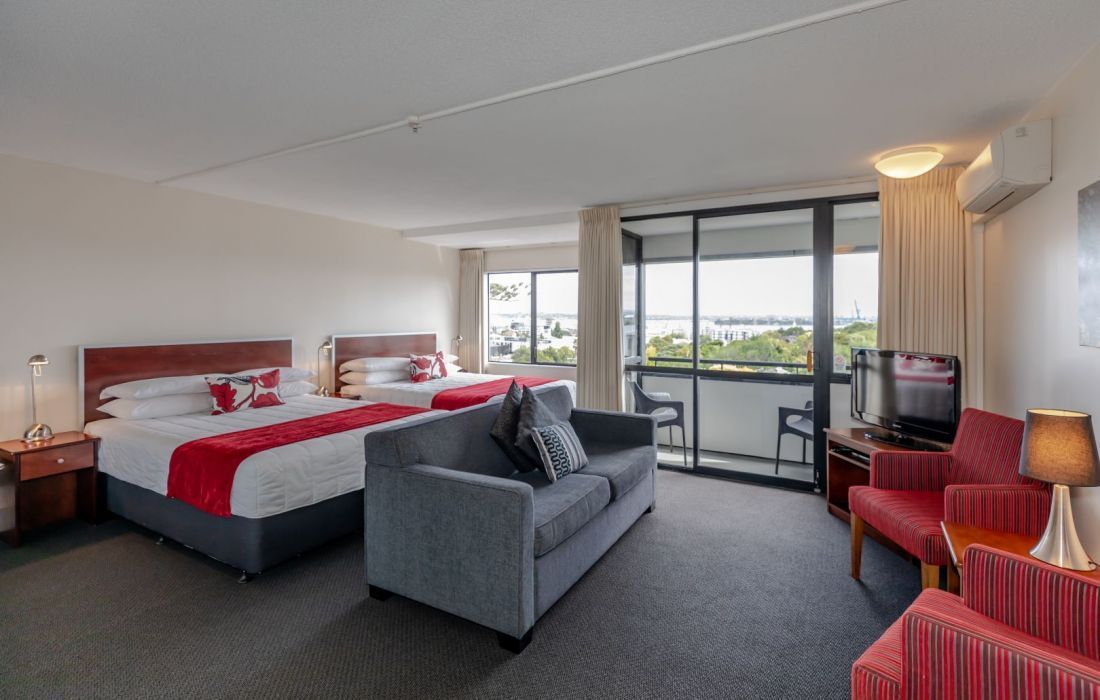 Hotel room with two beds, sofa, red chairs, and a balcony view through large windows