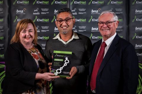 Three people in business attire holding an award plaque at a Kiwinet-branded event.