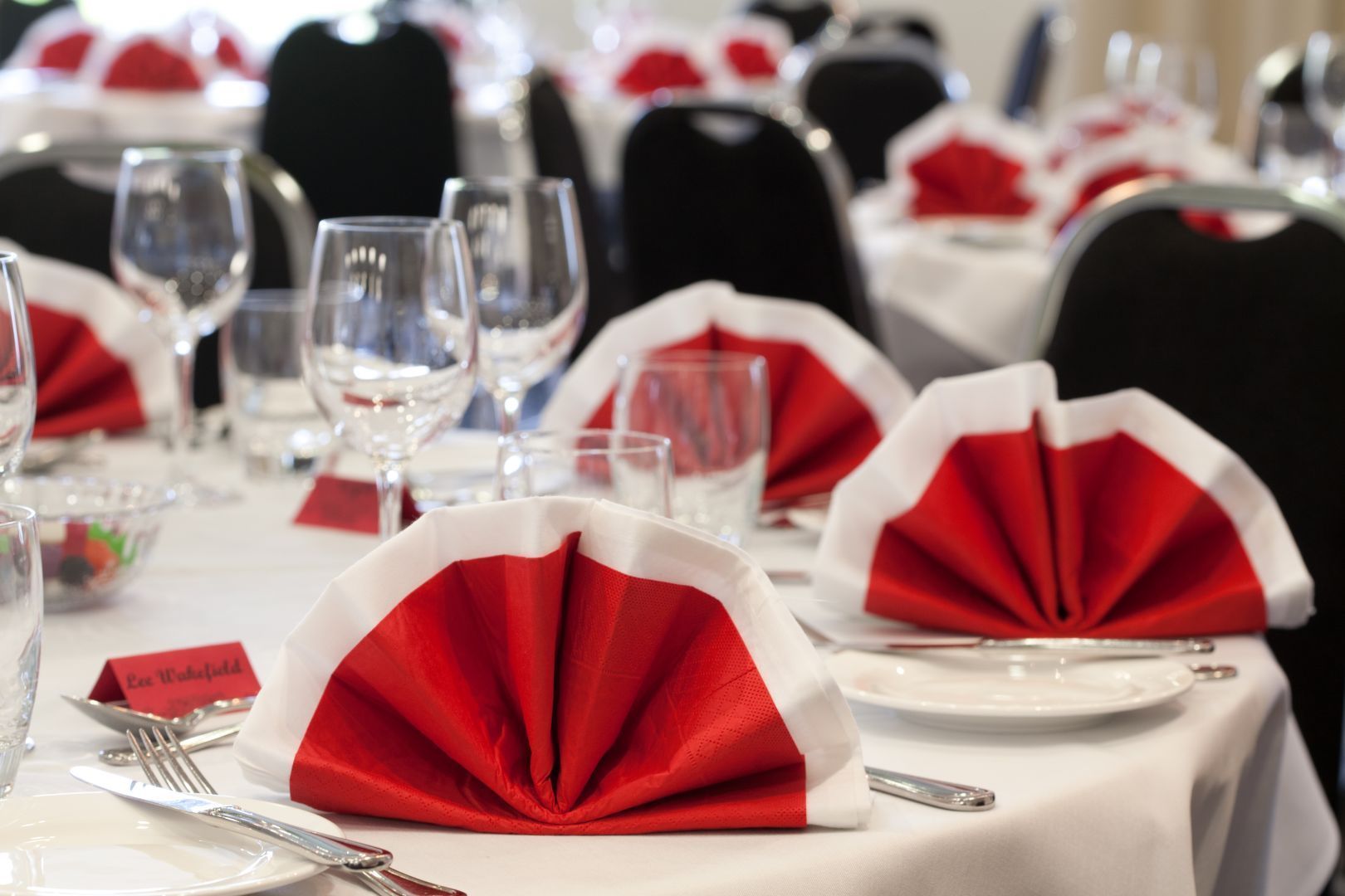 Banquet table set with red and white folded napkins, wine glasses, and white tablecloths