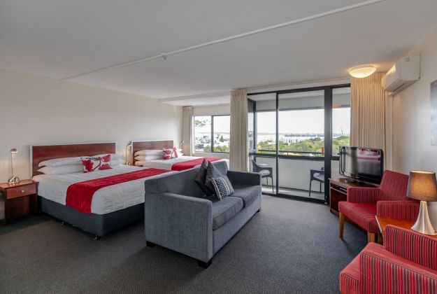 Hotel room with two beds, gray sofa, red chairs, and balcony view through large windows