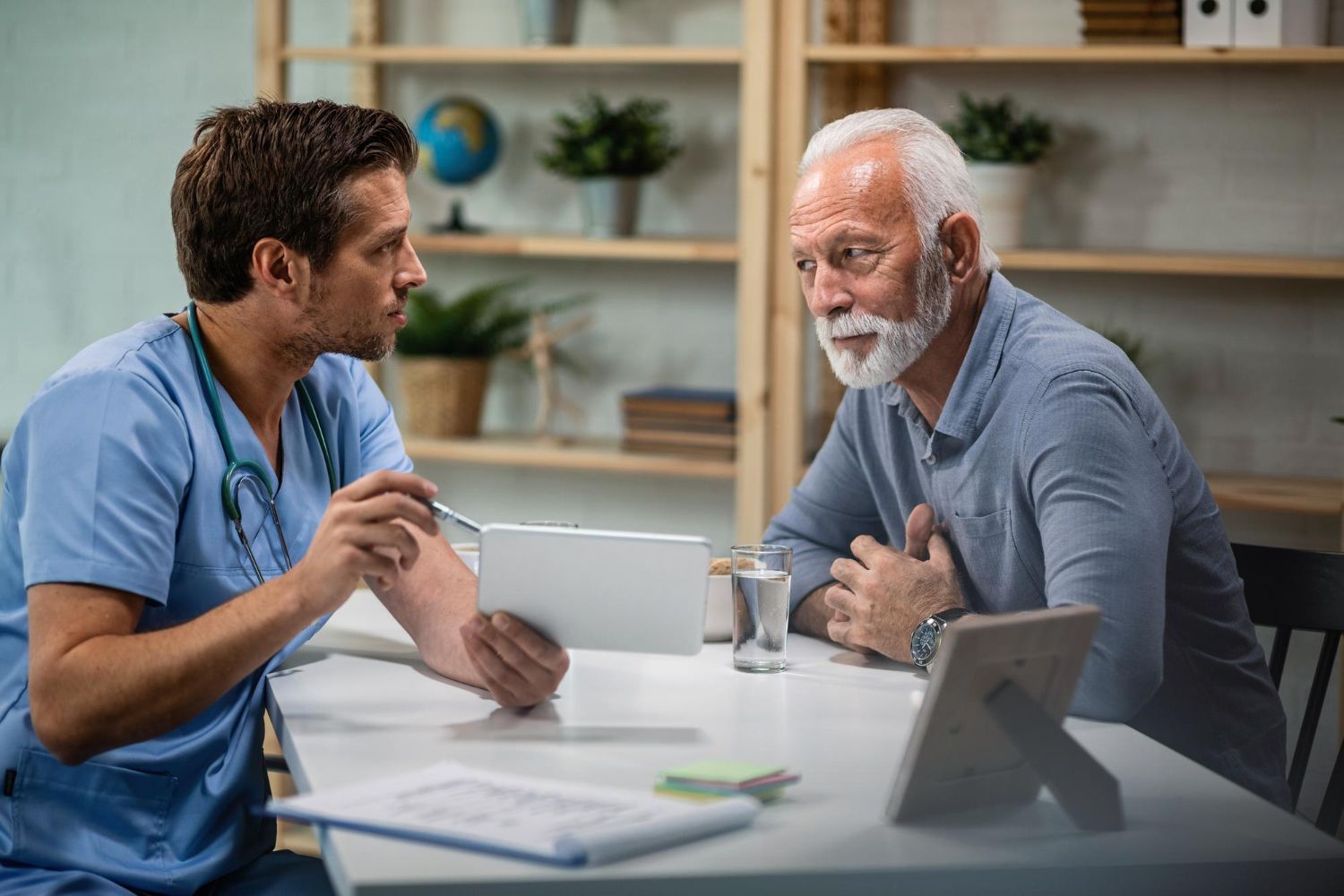 A doctor is talking to an older man who is sitting at a table.