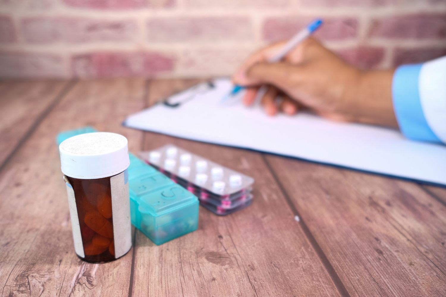 A person is writing on a clipboard next to a bottle of pills.