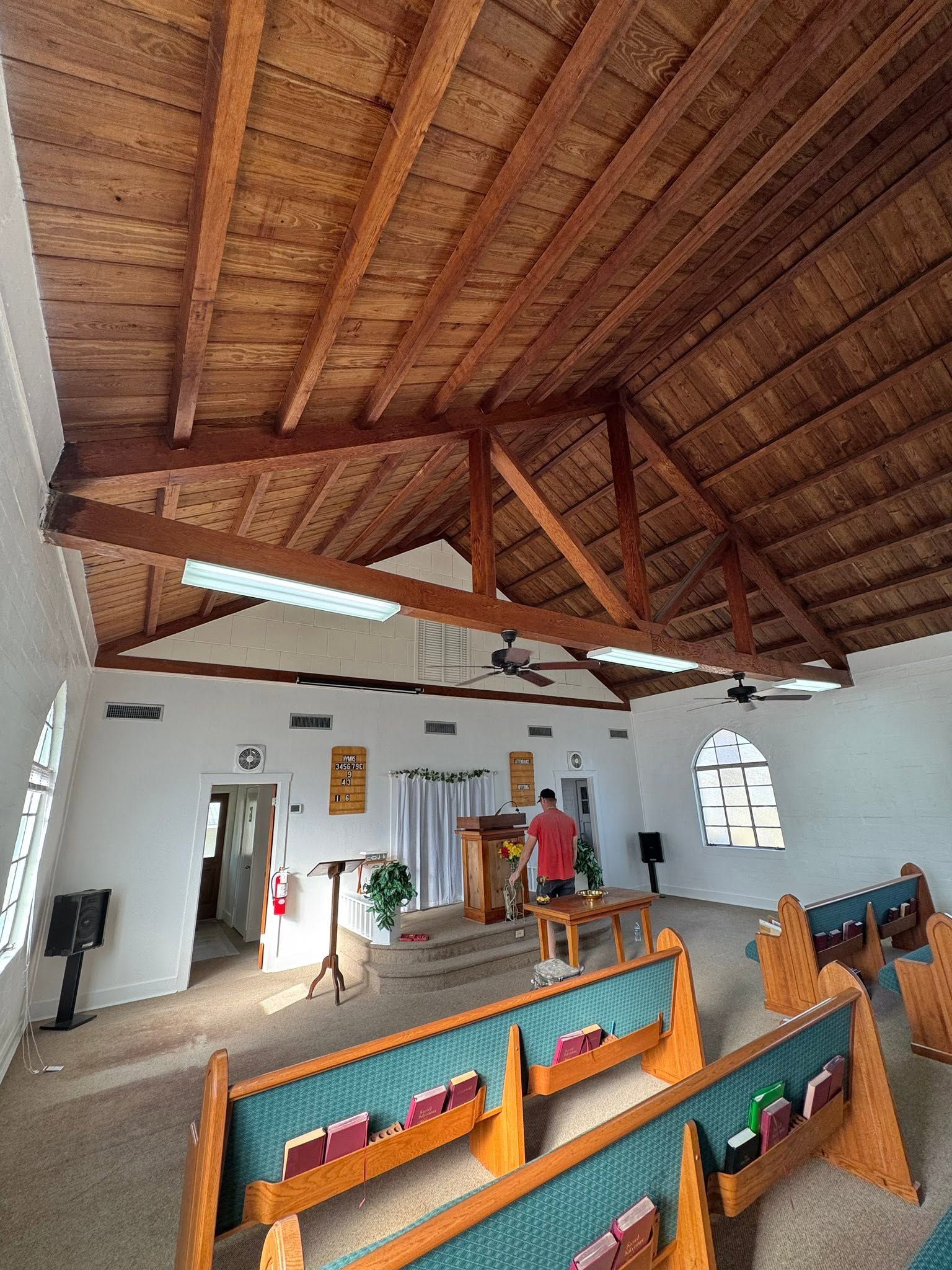 Church interior with wooden vaulted ceiling, pews, altar, and a few people near the front