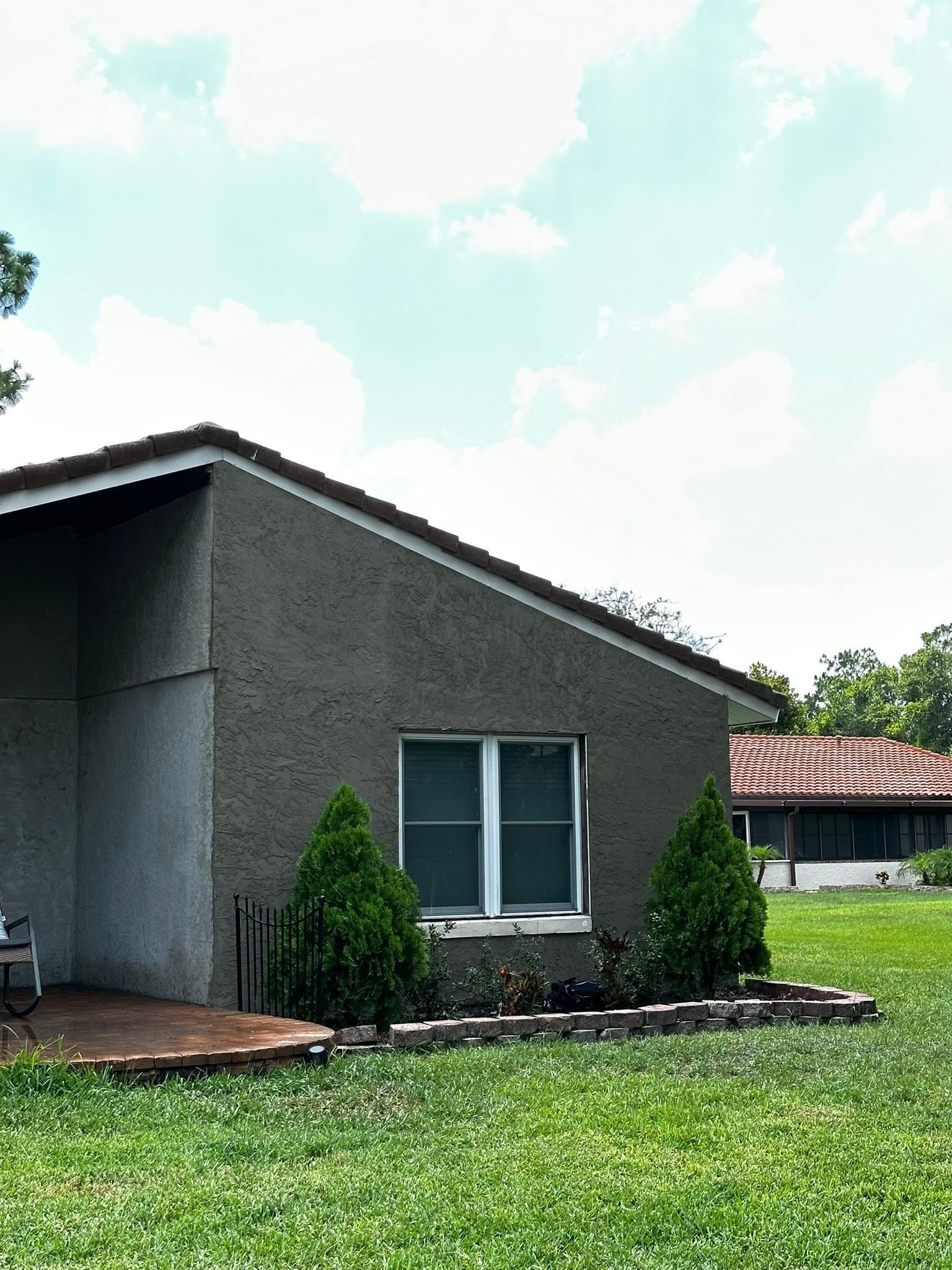 Gray house with a small front yard, shrubs, and a blue sky above