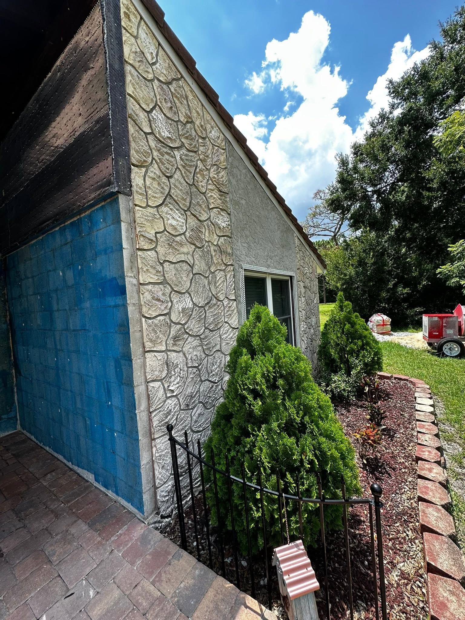 Stone house with blue side wall, small window, hedges, and a brick path in a sunny yard