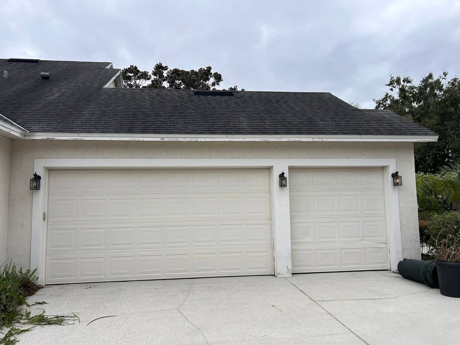 Two-car garage with white doors and a dark shingled roof on a house exterior