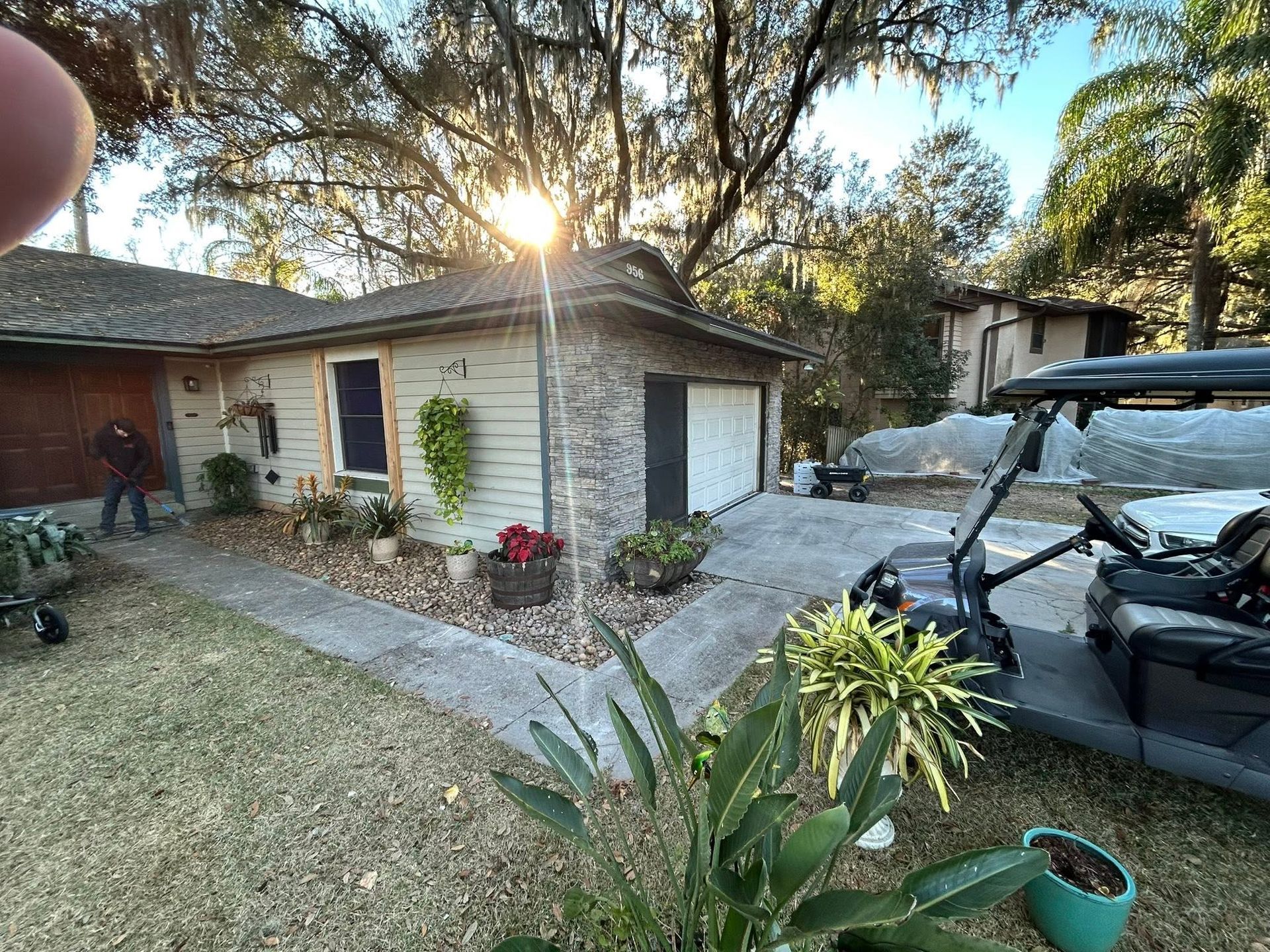 Single-story house with driveway, parked car, and sunset light in a leafy yard
