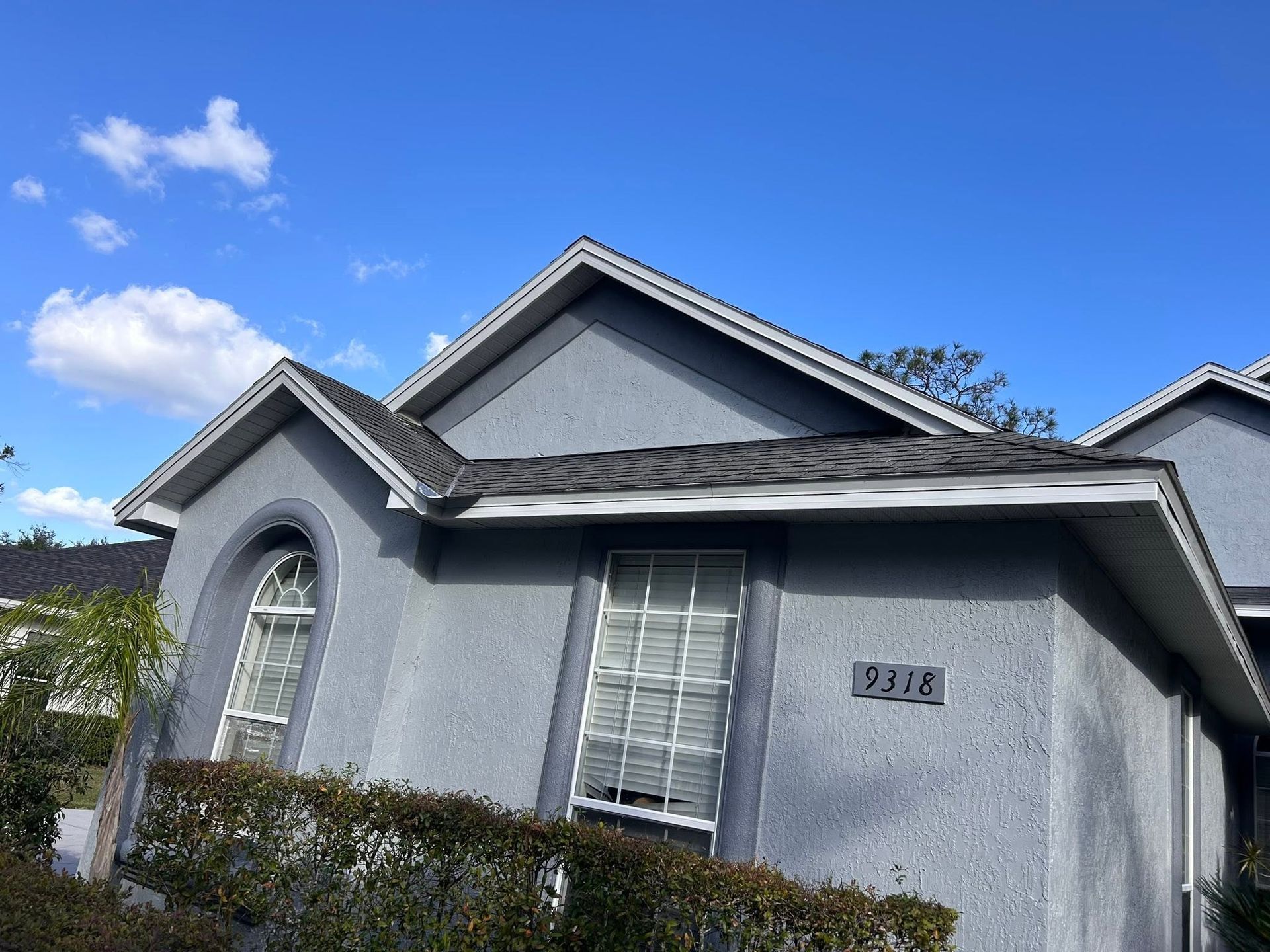 Gray house exterior with gabled roof, arched window, and hedges under a blue sky