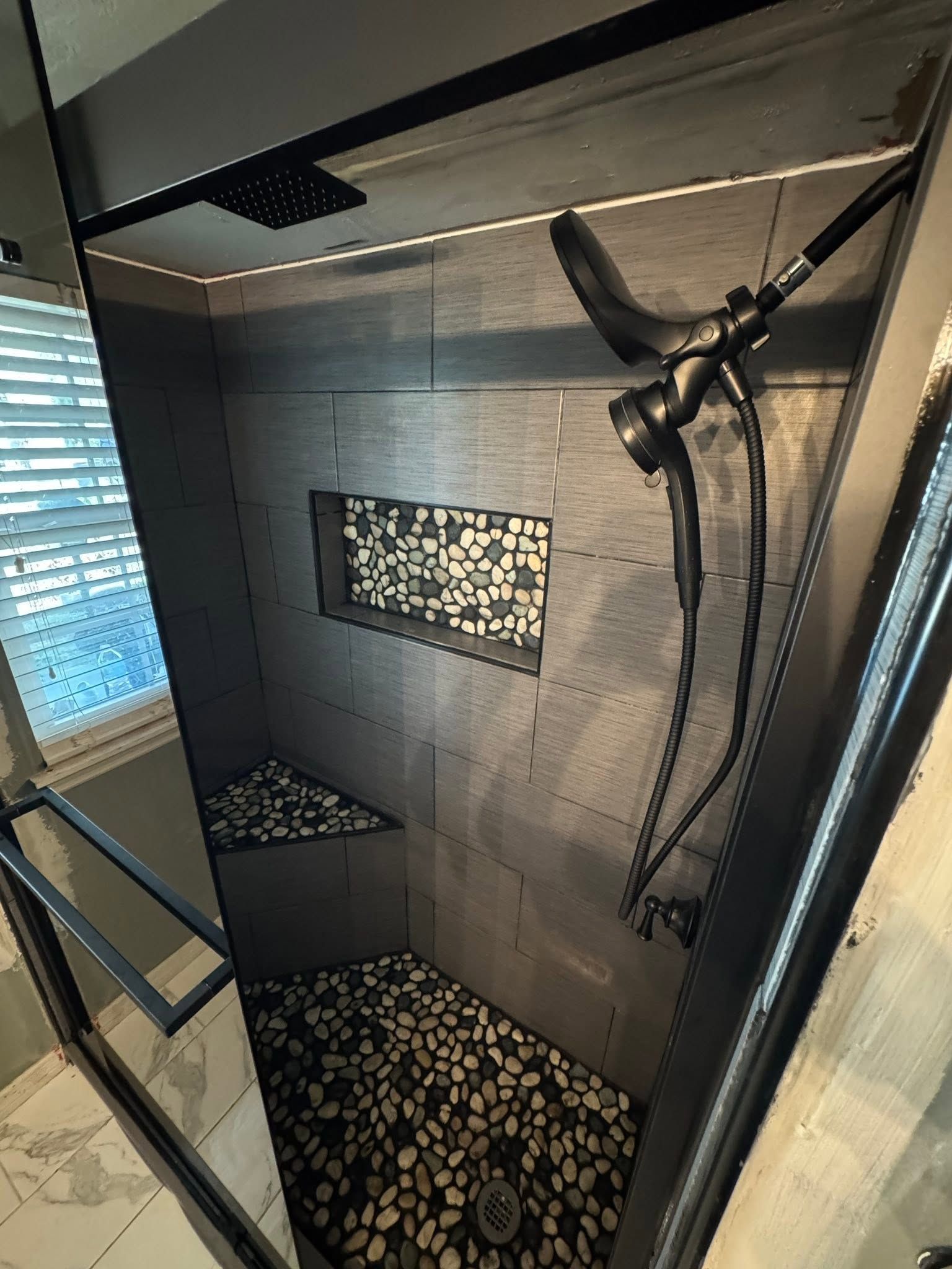 Modern shower stall with gray tile, pebble floor, and a wall-mounted rainfall showerhead.