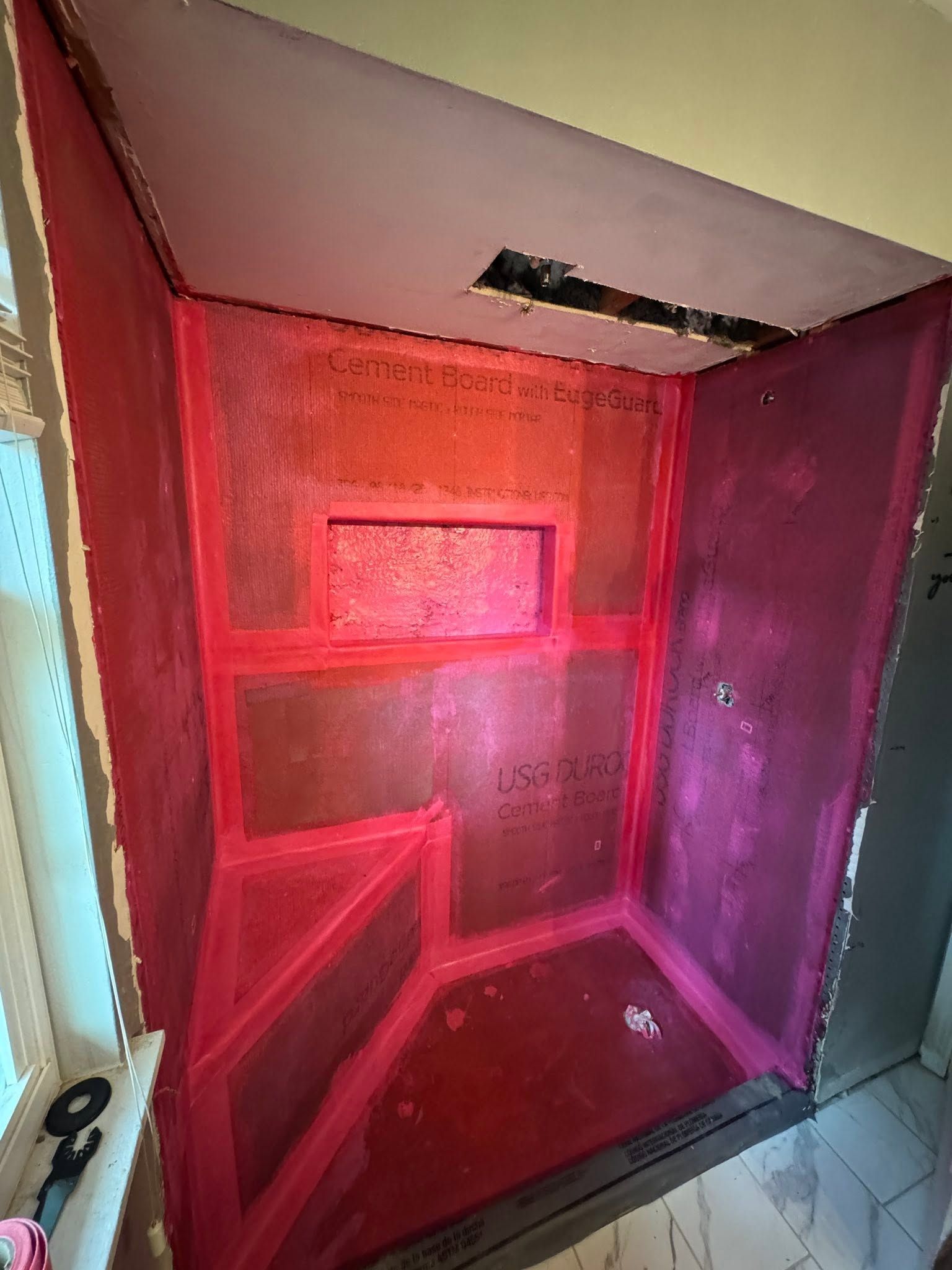 Red shower stall with pink mesh panels and a small ceiling vent, viewed from the bathroom doorway